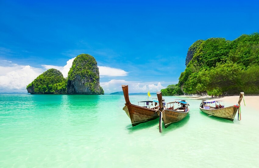 Thai fishing boats on quiet Phra Nang Beach with limestone cliffs
